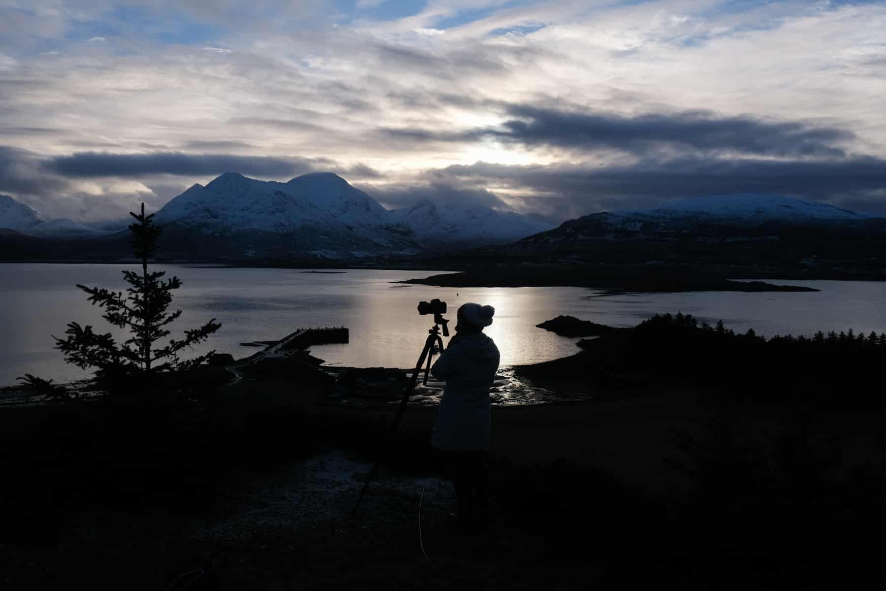 Photographer learning on the Isle of Rassay looking over to skye at sunset 